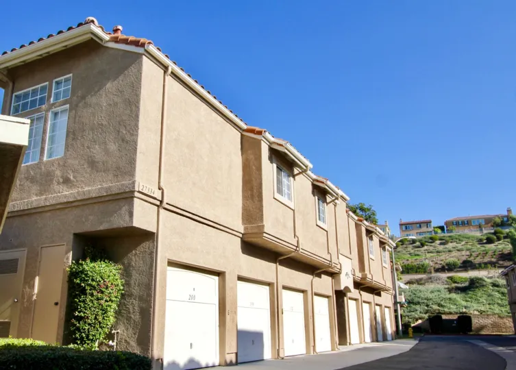 A tall hedge sits tucked into an indent in a tan building in the Village Niguel Terrace II community