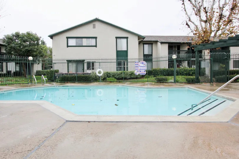 View of pool in Aliso Creek Villas in Lake Forest, California. Pool has handrail to assist with entry/exit of pool. Pool area is fenced.