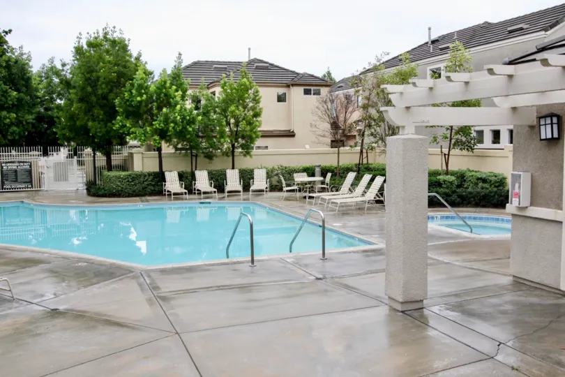 There are some white chairs nearby the swimming pool in the Brittany at Foothill Ranch.