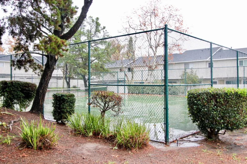 A green fence surrounds a large tennis court at the Richwood community in Lake Forest, California.