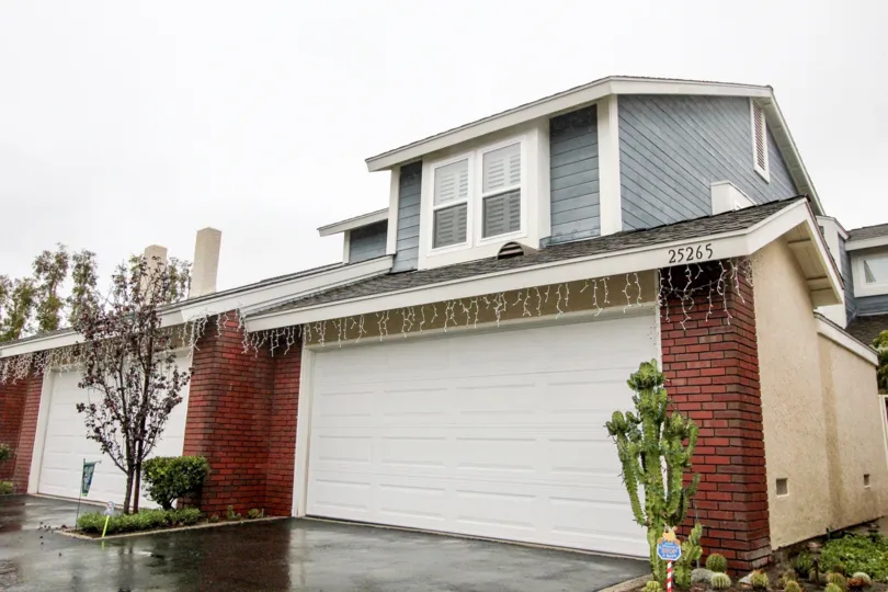 A black, shiny wet driveway sits in front of a garage in the San Remo Villas community