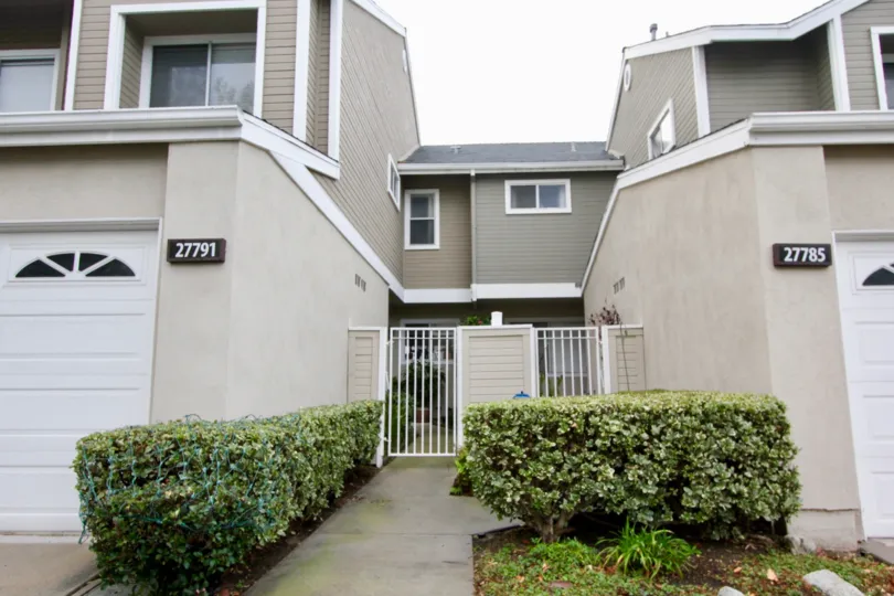 way in between the two house in colony having green bushes both the sides.