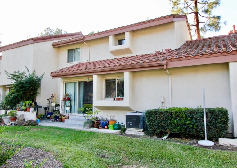 A house with colourful pots of plants and grass and also two windows with sandal colour.