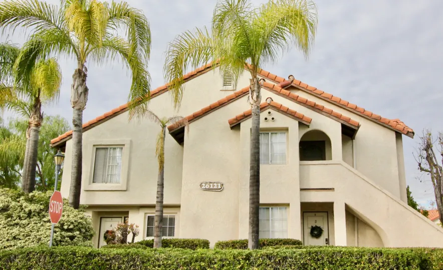 A large home with four large palm trees, two floors on a cloudy day