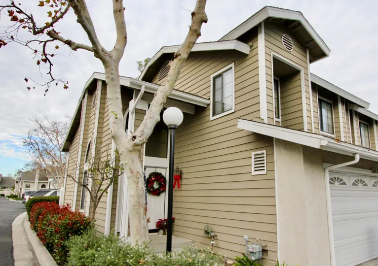 A corner view of a tan house in Mission Viejo, California, including the garage door, side entrance and other homes in the background.