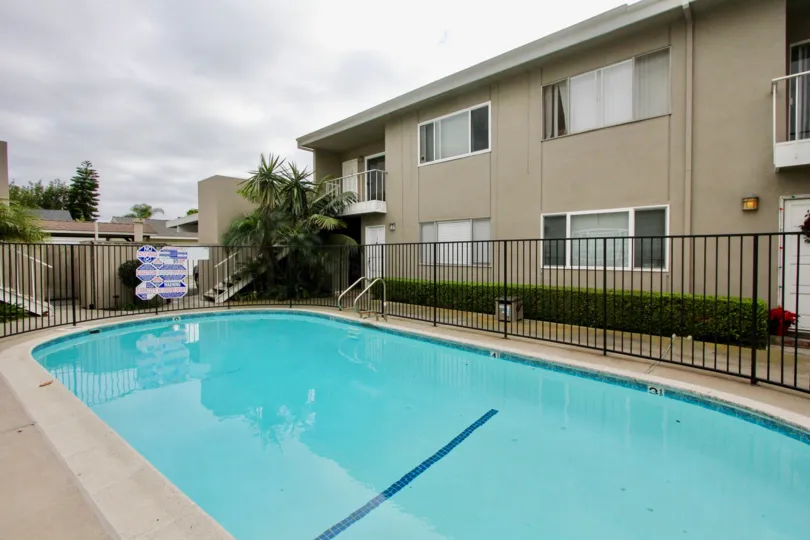 A cloudy day in the Newport Garden Villas with a swimming pool nearby a building.