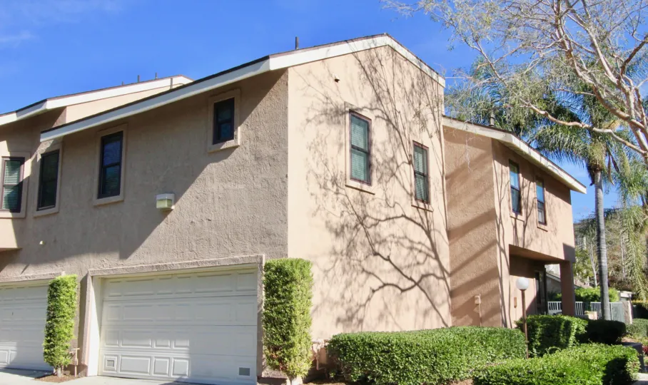 A beige house in Canyon Glen with trimmed bushes and a garage