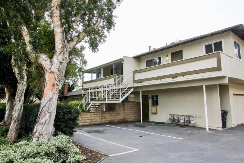 A beautiful light yellow and green building in the Criterion with big trees, shrubs, staires near the road.