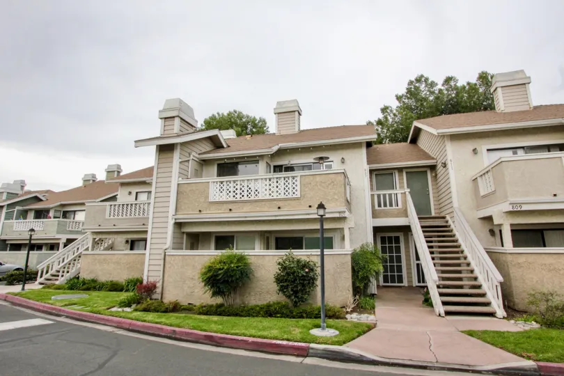 A beautiful light yellow and white building in the Fletcher Avenue with big trees, small beautiful plants, shrubs, green grass, staires near the road.