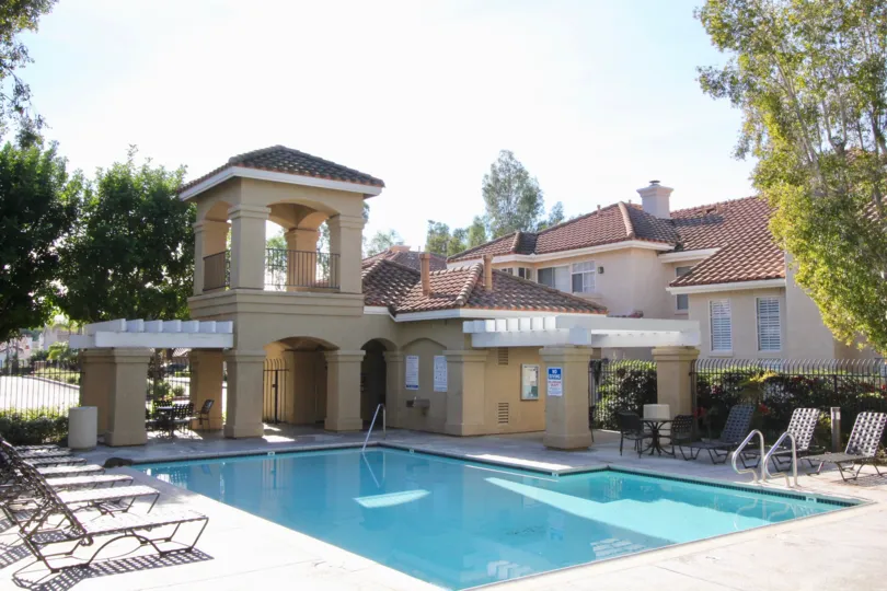 The swimming pool in the Montevista with the big light yellow and white color buldings, resting chairs, small trees, big trees.