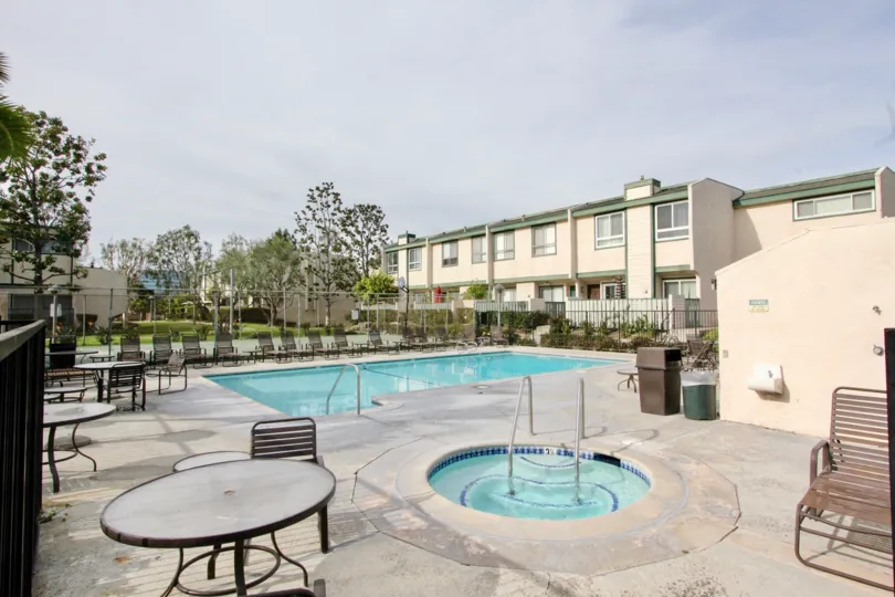 The pool and hot tub in Park Terrace Village with chairs and tables of a cloudy day