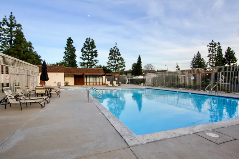 The pool and lawn chairs in the Smoketree Orange Townhomes community with a fence on a sunny day.