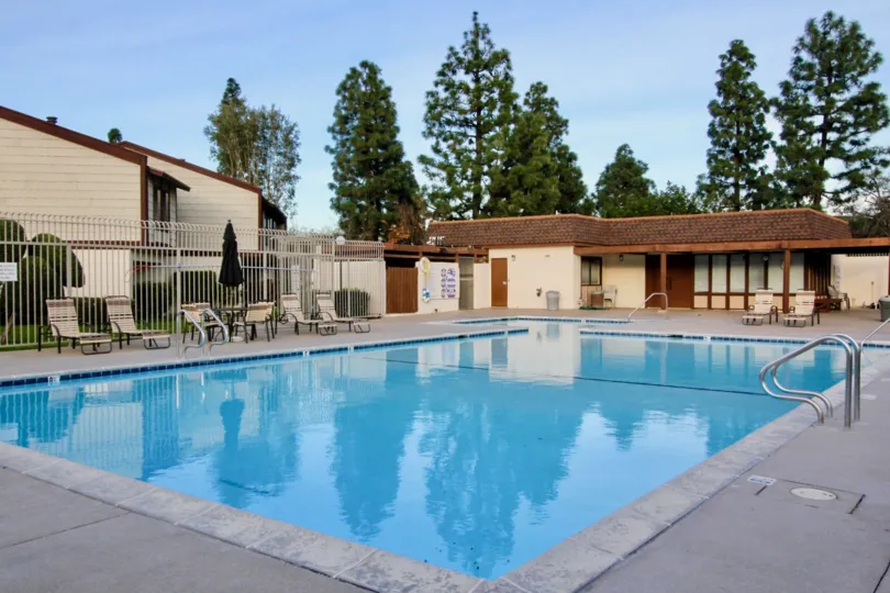 A pool in Smoketree Orange Townhomes surrounded my chairs and a fence on a sunny day