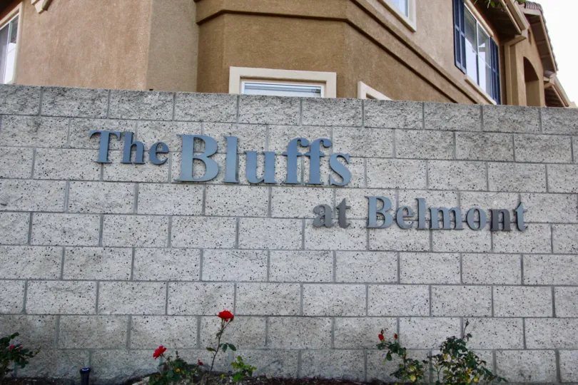 Brick wall with named of The Bluffs at Belmont, in blue, mounted on the wall with an apartment in the background