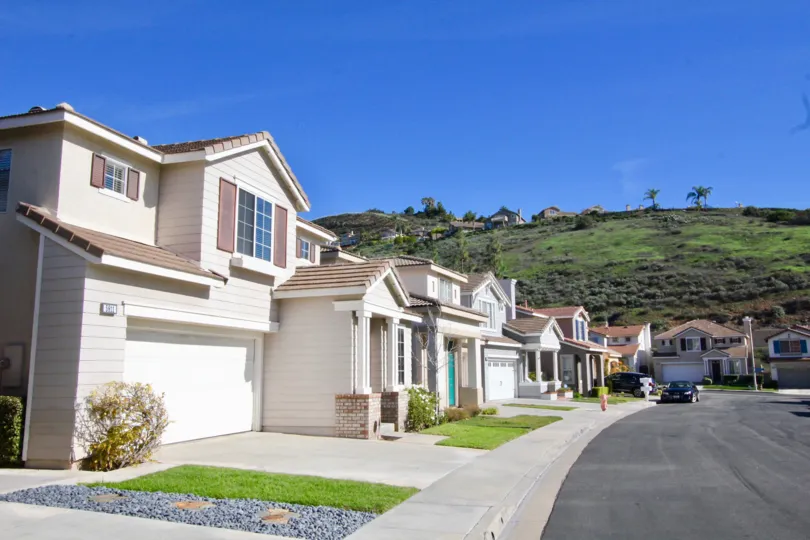 The white and grey color big buildings near the hilly area in the The Village with the beautiful ornamental green grass, shrubs, trees near the road.