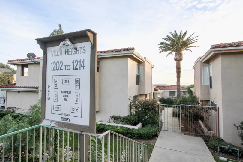 A sign and gated entrance to the Villa Heights community with bushes and palm tree