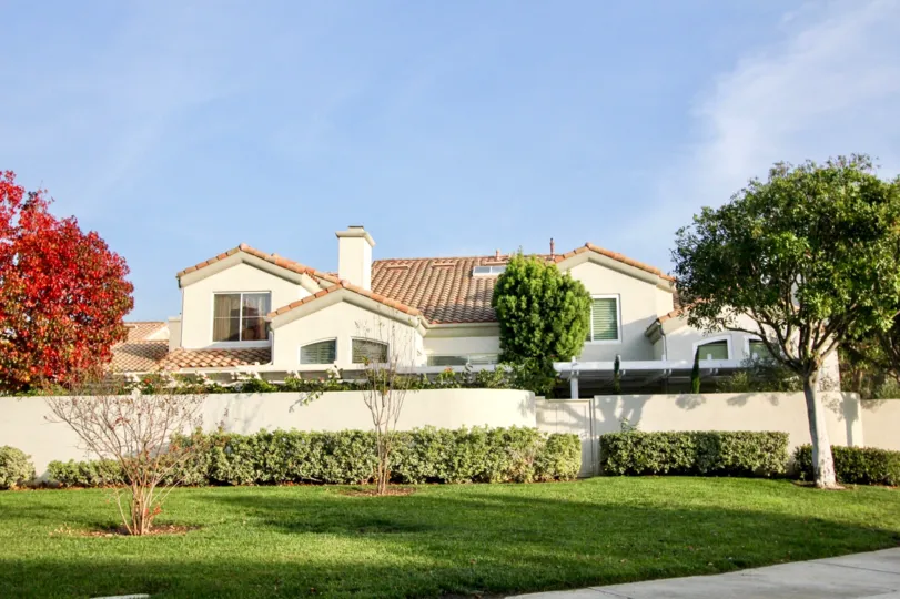 A lush, full red and green tree sits in front of a townhome in the Alicante community