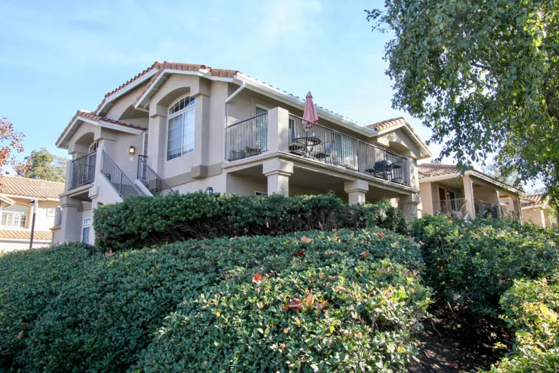 Multi floor house with pillars and wrap around deck with trees and shrubs.