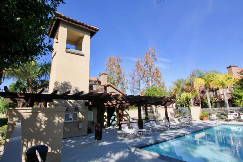 The poolhouse, lounge chairs and pool shaded by trees in the Brisa del Lago II community in Rancho Santa Margarita, CA