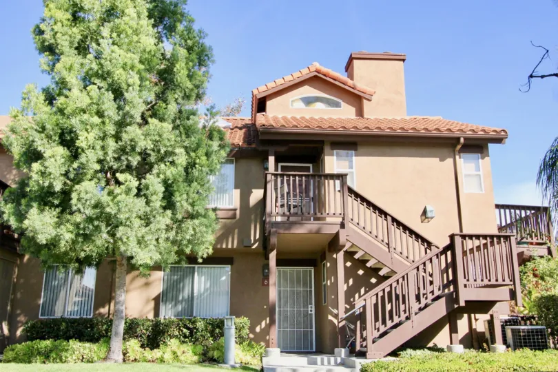 A sunny day by a Brisa del Lago house with multiple stories, a stairway out front, and a big tree in the lawn