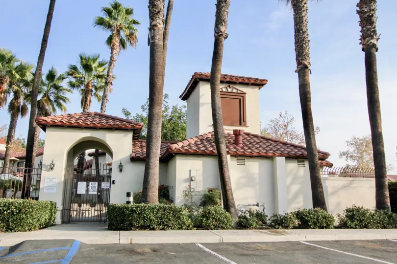 Tall palm trees in front of gated building with red roofs