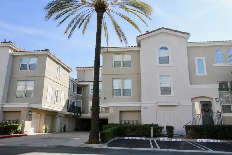 A large residential building with a large car park and a palm tree