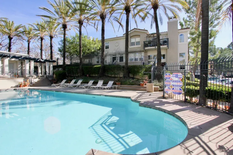 A sunny day by a Cierra Del Lago pool with apartments and palm trees behind it