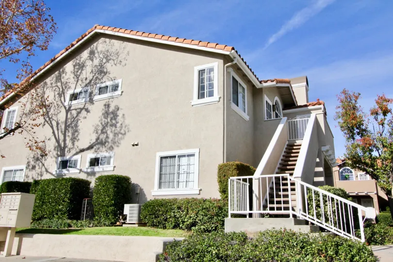 A two-storey residence with exterior staircase and grayish paint in the Las Flores community.