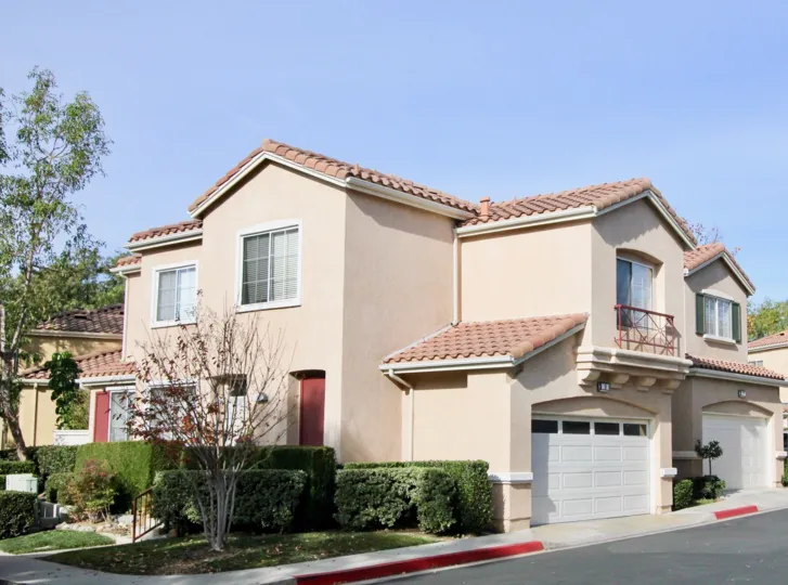 View of a residence located in Los Albanicos in Rancho Santa Margarita, California. Front entry surrounded by bushes. Maple tree outside of residence.