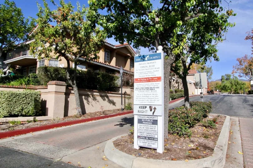The entrance to Mission Courts community with a neighborhood rules and regulations sign and magnolia trees