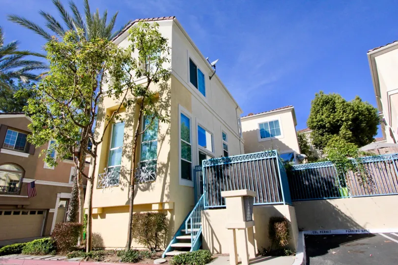 Street level view of the Montana Del Lago community with blue wrought iron, trees and parking