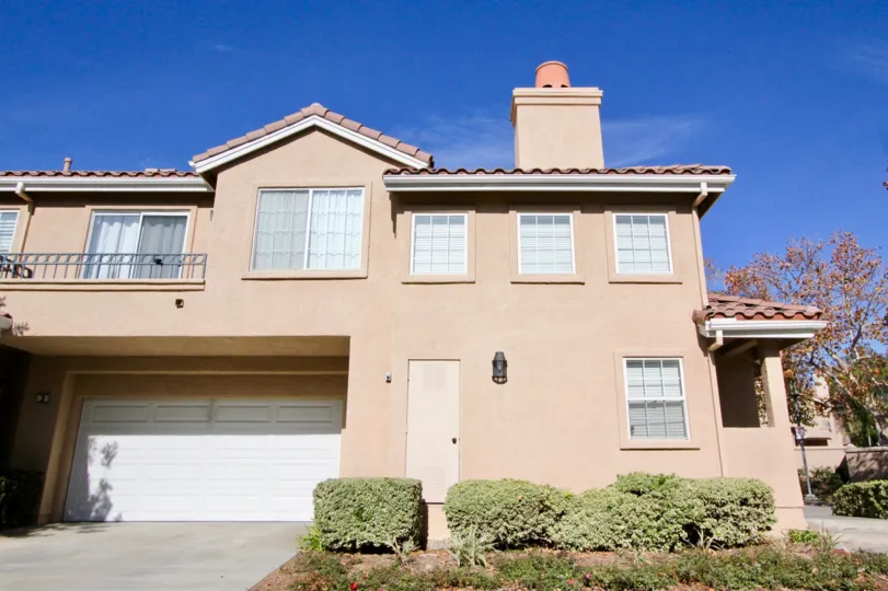 View of a residence located in Sonoma Court in Rancho Santa Margarita, California. Upstairs balcony and two car garage. Bushes around outside of residence.