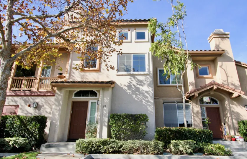 A sunny day at a Tierra Linda duplex with bushes in front of it and in between each walkway, along with a tree on one side
