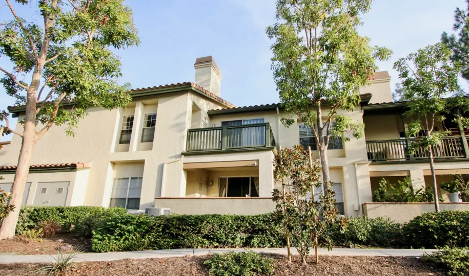 A mostly sunny day by a Tijeras Creek Villas complex with trees, bushes, and dirt around the building