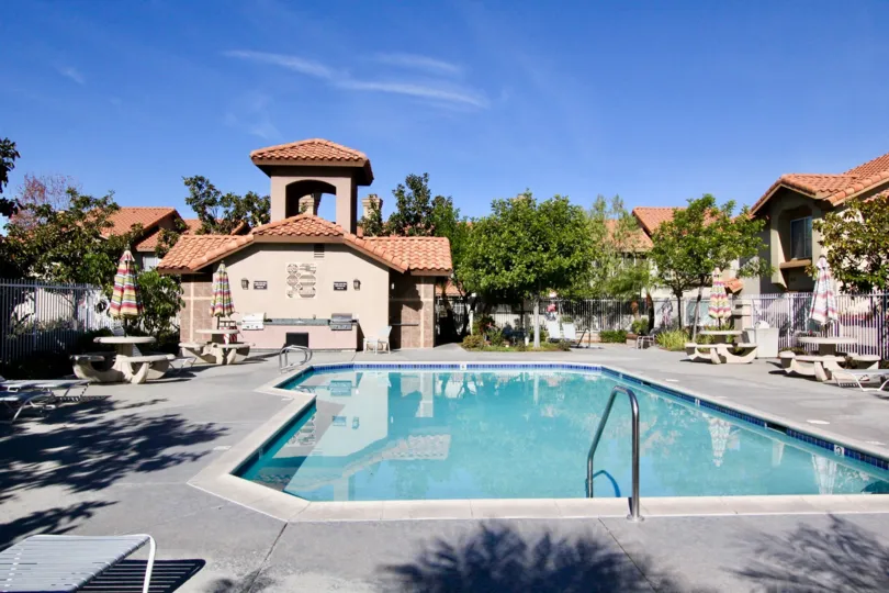 A sunny day by a pool in Vista La Cuesta with tables, umbrellas, and a wholesome landscape all around