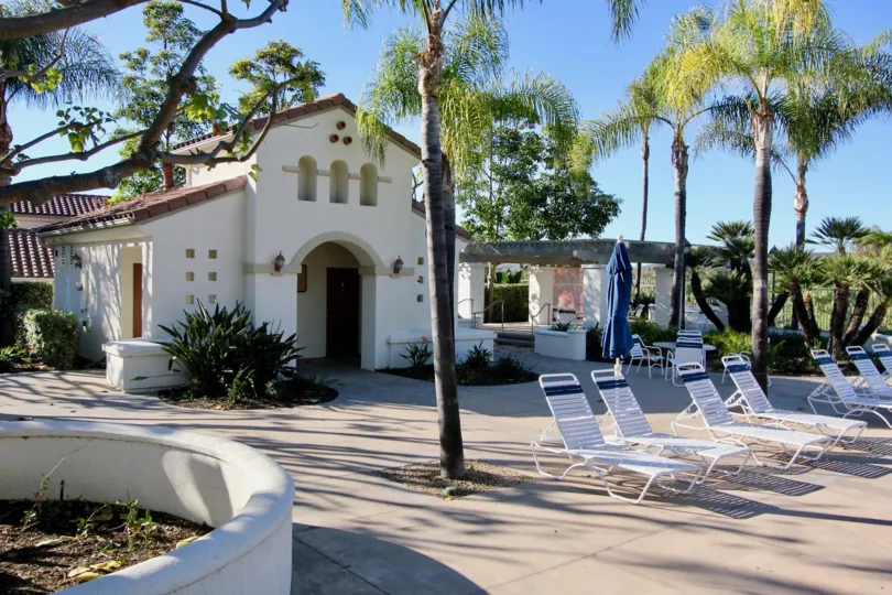 A beautiful house and it is surrounded with a set of trees and there is a set of chairs to have relax.