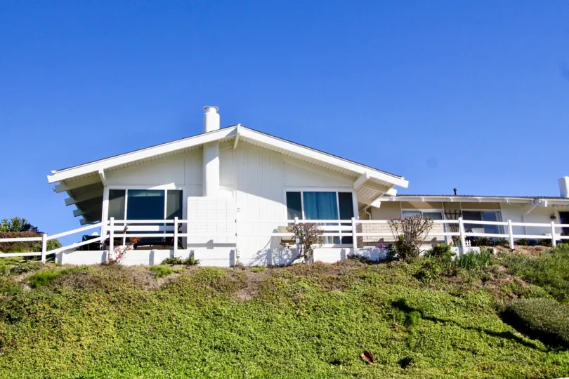 A white wooden fence sits near a house on a hill at Colony Cove