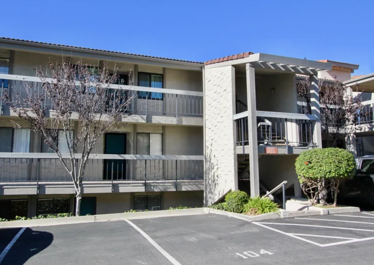 A Two Floor Building. A Small Tree In Front of Main Gate, and it has a plenty car parking space.