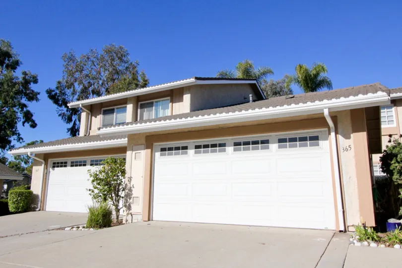 A small flower patch with bushes sits between two garage doors at Mira Costa Villas