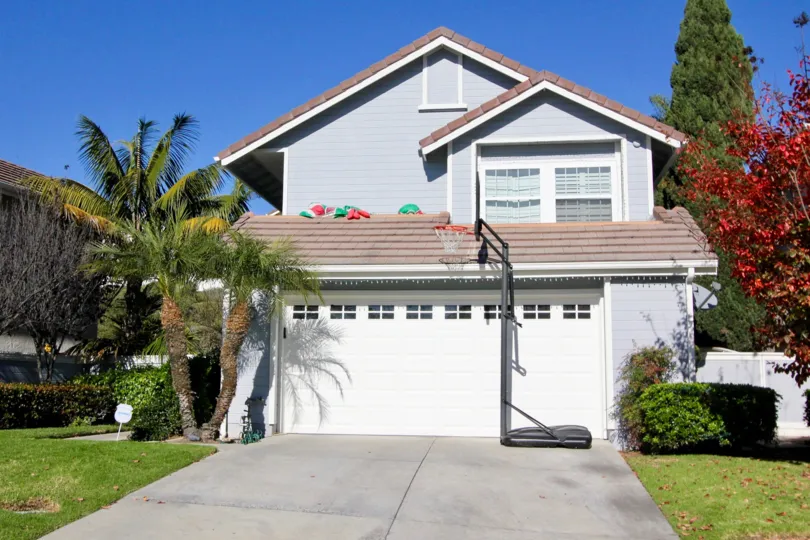 A beautiful house with a garrage at the front and it is surrounded by trees and a red coloured tree