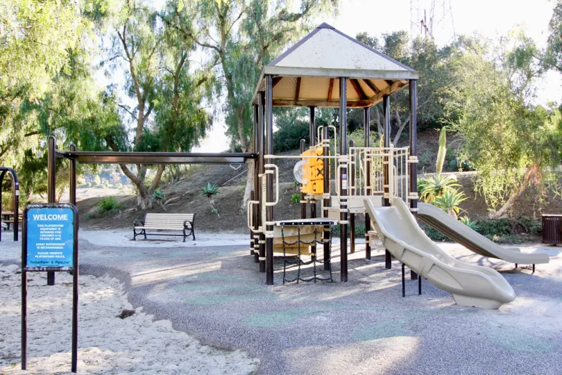 children's playground with white slides, bars, ropes, and bench for adults