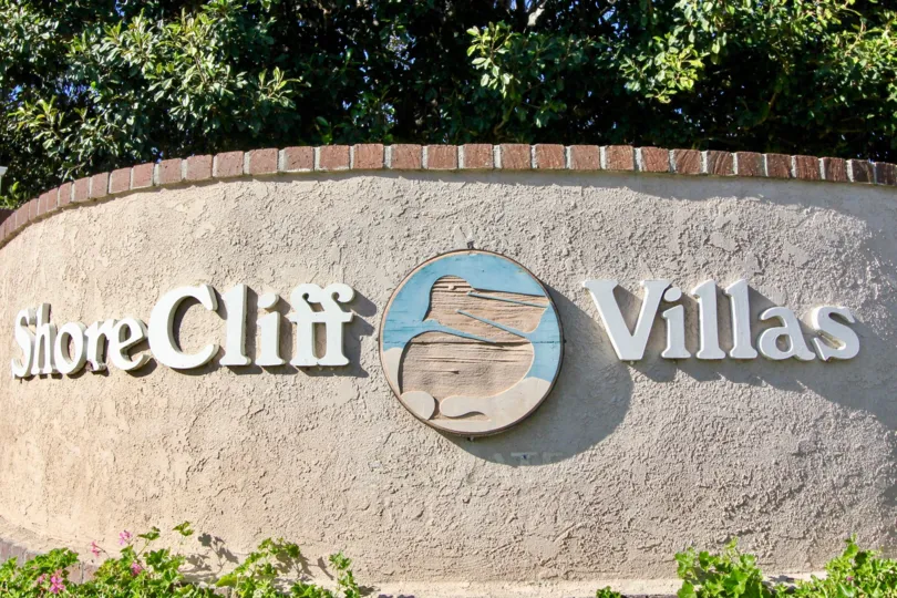 a sunny day in the shore cliff villas with a wall that has the name of the community with a symbol in it