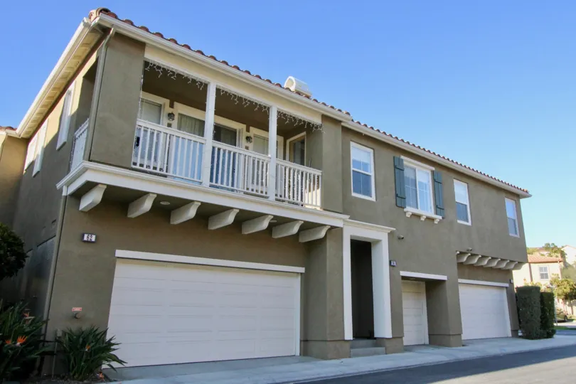 a sunny day in the verano with a house that has plants on either side and a balcony on the left side of the building