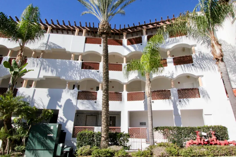 A Three Floor Building Contains Some tall trees in front of the Main Gate, and has a small garden.