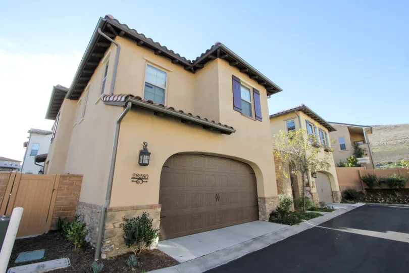 A sunny day by a Campanilla house, painted with the color combination of beige (sides & main areas) and brown (doors, window sides, roof)