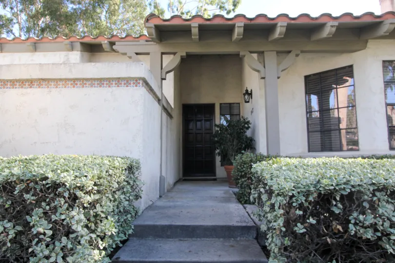 A view of the front porch, doorway, hedges, and windows, of a home in San Juan Capistrano, Capistrano D'oro district.