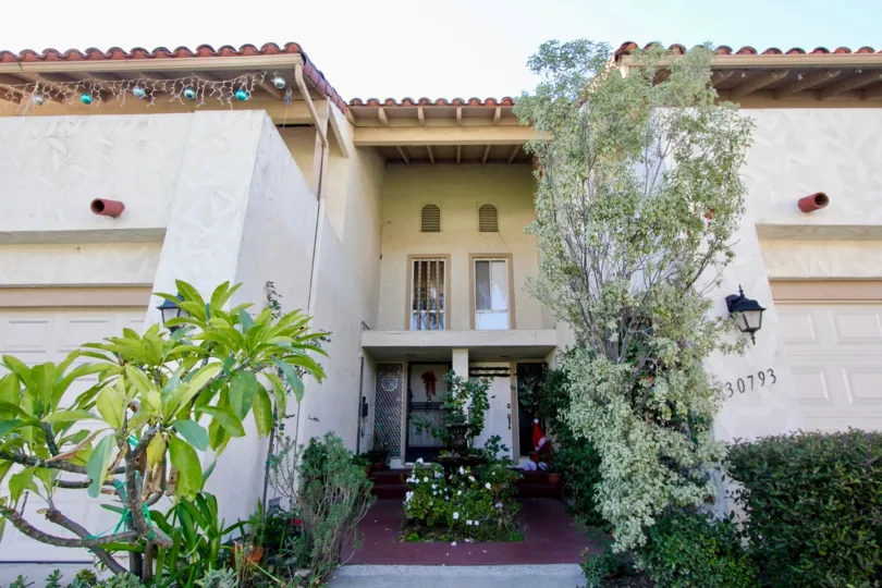 A sunny day by a Casitas Capistrano duplex with Christmas decorations on both front doors and random plants scattered about