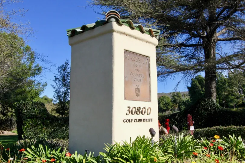 The entrance post to the Marbella Golf and Country Club with flowers, trees and greenery in San Juan Capistrano, CA