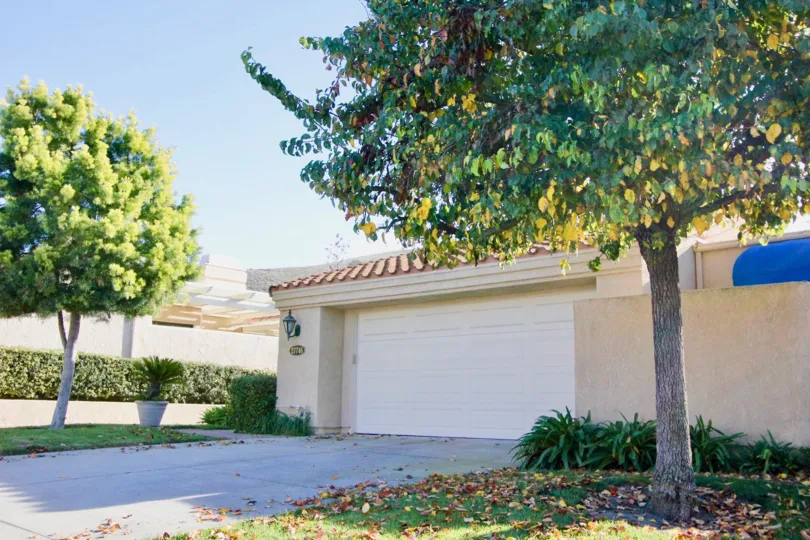 A sunny day by a house in the Mesa Verde area with a garage and trees on each side of the driveway