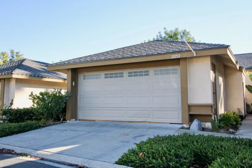 A sunny day by a Mission Point house with a couple potted plants next to the garage door and with other plants in front of it